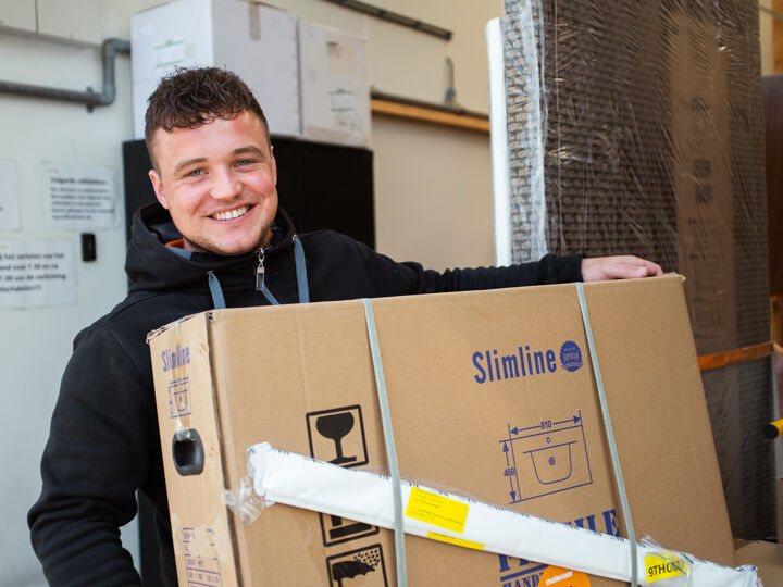 Monteur Ruben lachend met kartonnen doos in magazijn