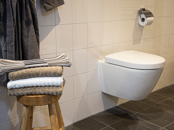 Hangend toilet wit op tegelmuur met bruine handdoeken op houten krukje